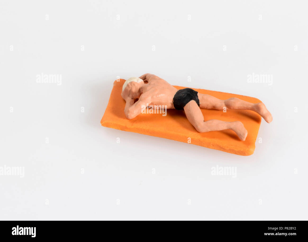 Miniatur Mann in Badekleidung Liegen zum Sonnenbaden an einem hellen orange Handtuch am Strand in ein Konzept von einem Sommer Urlaub auf Weiß mit Kopie isoliert Stockfoto