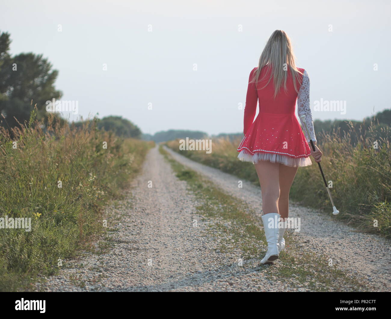 Blonde Teen Majorette Mädchen Twirling Baton draußen im roten Kleid Stockfoto