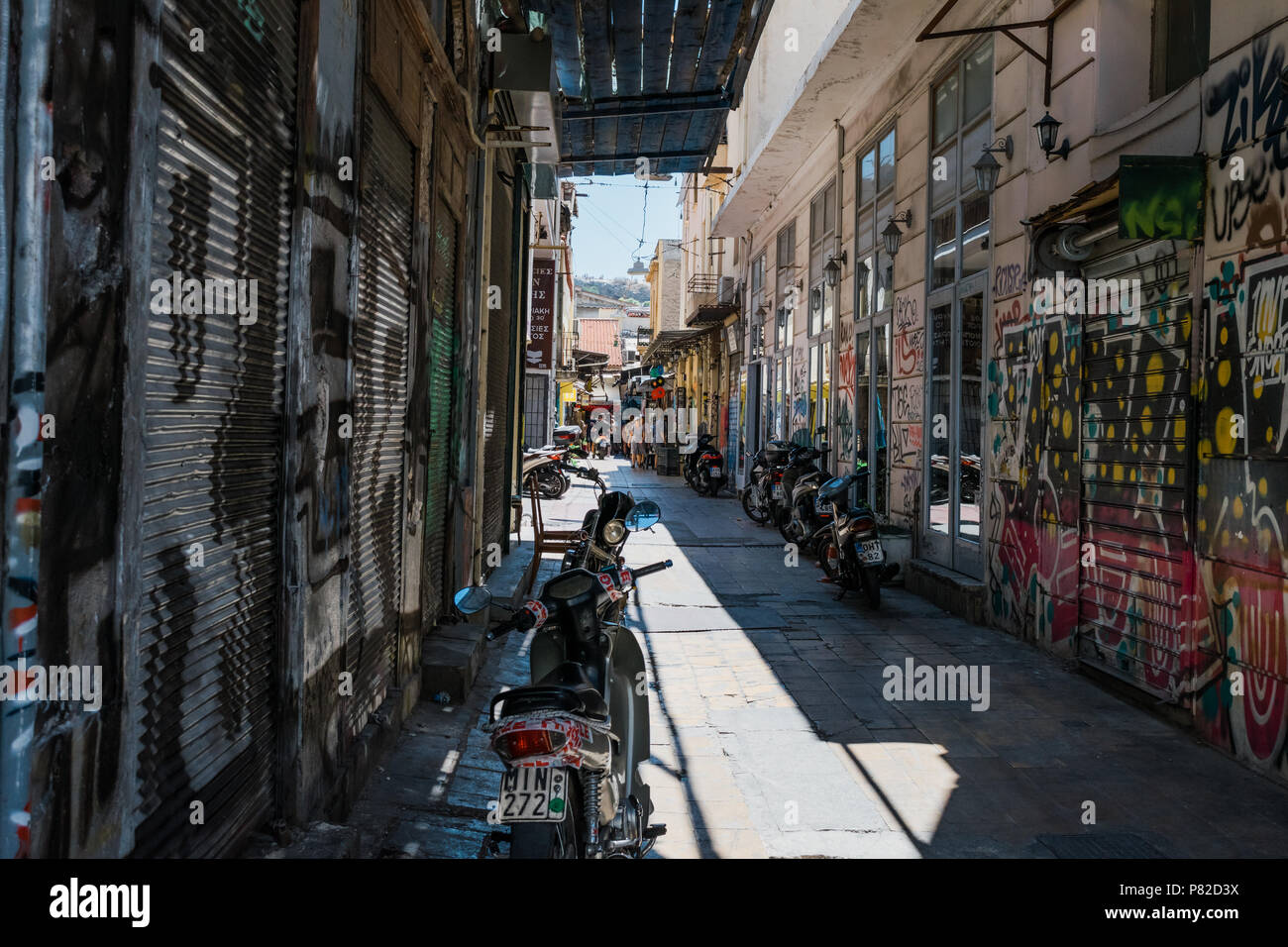 Motorräder in schattigen Fliesen- Straße von Athen, Griechenland. Mit Graffiti an den Wänden und Rollläden. Stockfoto