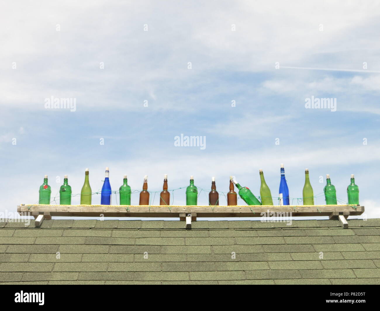 Zehn grünen Flaschen (plus ein paar andere) steht in einer Reihe an der Wand vor einem Blauen und bewölkter Himmel; und die Kinderlieder sagt, man begann zu fallen Stockfoto