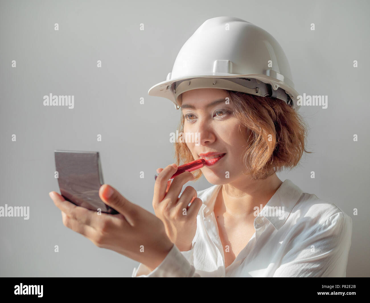 Schöne asiatische Frau Ingenieur curly kurze Haare tragen weiße Helm und weißem T-Shirt Make-up mit rotem Lippenstift, berufstätige Frau Konzept. Stockfoto