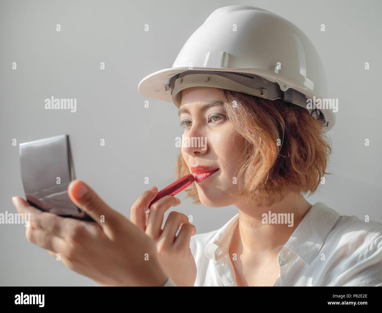 Schöne asiatische Frau Ingenieur curly kurze Haare tragen weiße Helm und weißem T-Shirt Make-up mit rotem Lippenstift, berufstätige Frau Konzept. Stockfoto