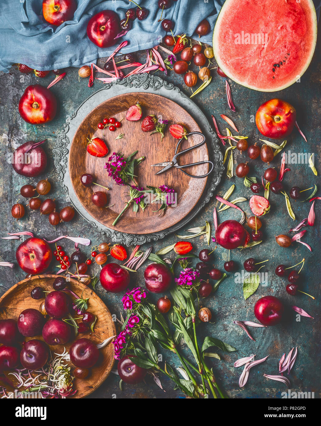Verschiedene Sommer Beeren und Früchte auf rustikalen alter Küchentisch mit Blumen und Platten, Ansicht von oben, flach. Saisonale gesunde lokale organische Nahrung und ea Stockfoto
