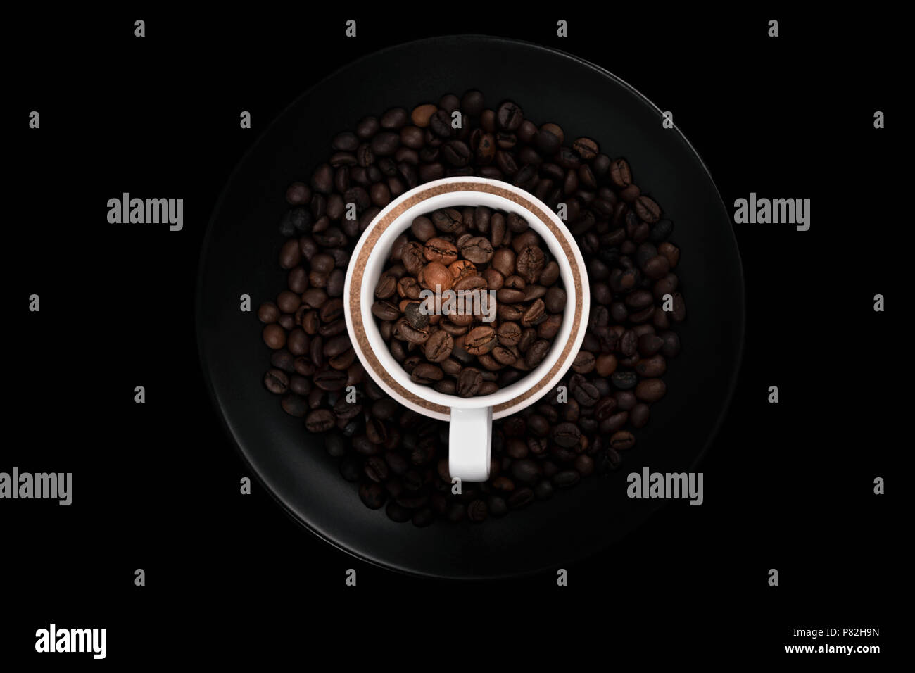 Weiße Tasse voller Kaffeebohnen auf schwarze Platte mit gerösteten Kaffeebohnen gefüllt. Mit negativen Raum auf schwarzem Hintergrund. Stockfoto
