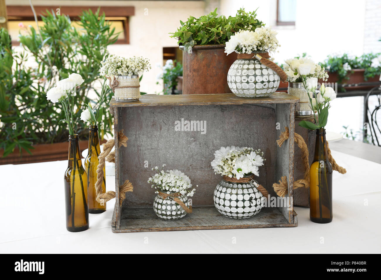 Florale Komposition von rein weißen Blüten in großen Flaschen und passende Weiß gestaltete Blumentöpfe, Vasen auf einem urigen freistehende Holzregal mit p Stockfoto