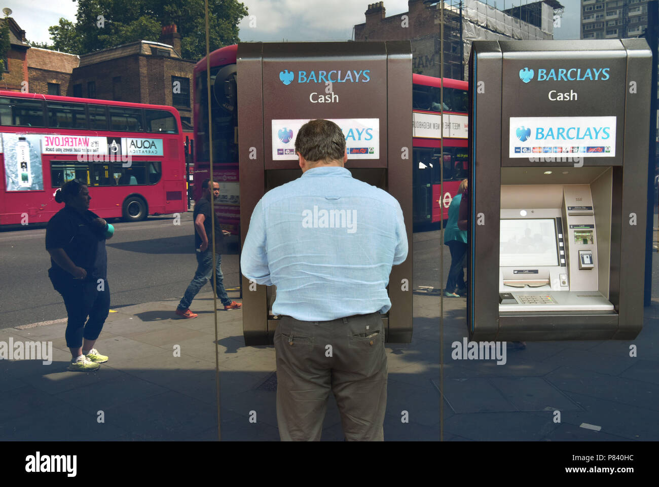 Menschen in das Fenster wider, Spaziergang, vorbei an die Bank Barclays, während ein Kunde die ATM in Notting Hill, London verwendet. Stockfoto