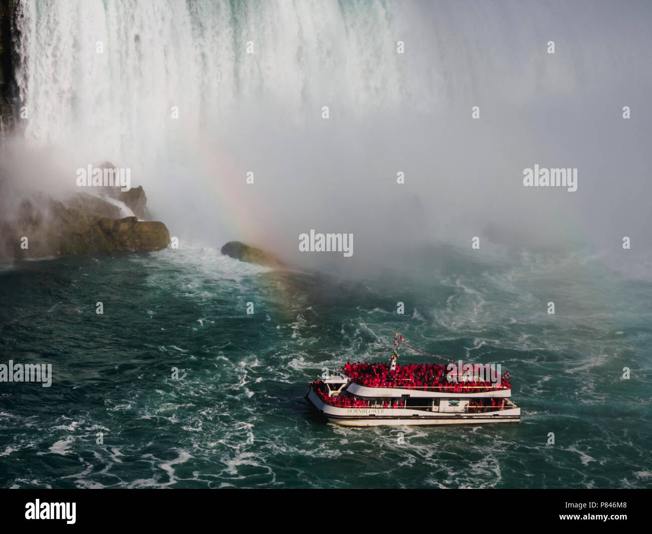Hornblower voller Touristen vor American Falls, Niagara Falls, Kanada auf einem klaren blauen Himmel Tag mit einem Regenbogen Stockfoto