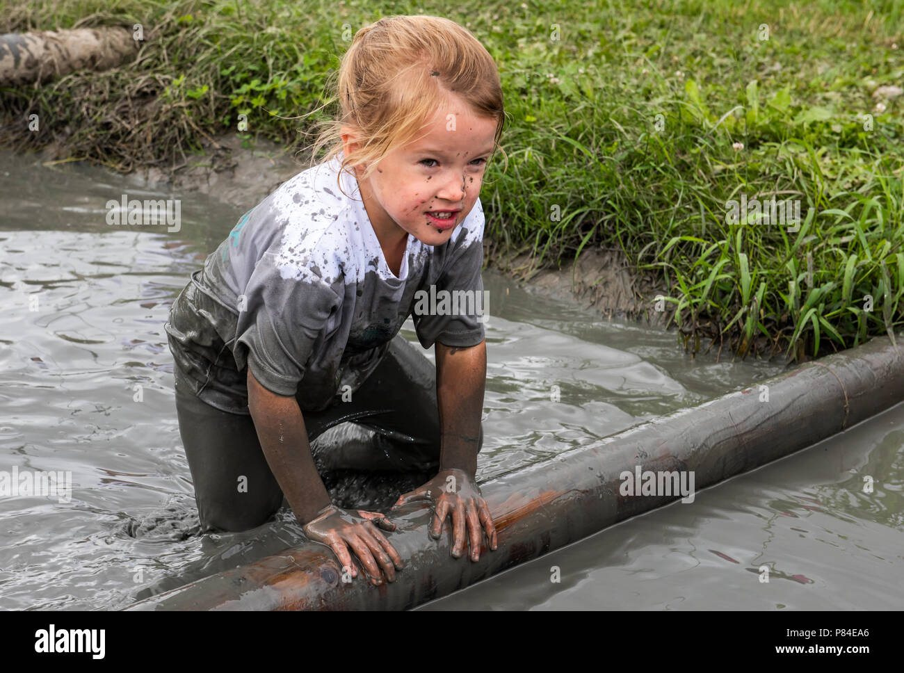 Biddinghuizen, Niederlande - 23. Juni 2018: Kind während einer mudrun (mudraise) im Schlamm und im Wasser klettern einen Baumstamm. Stockfoto