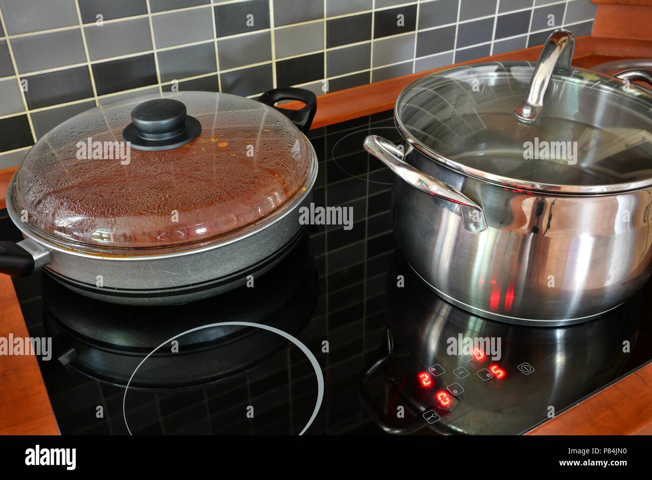 Schwarze Küche Induktionsherd mit Edelstahl Topf und Pfanne. Kochen in Töpfen auf Küche Herd mit modernen Fliesen. Stockfoto