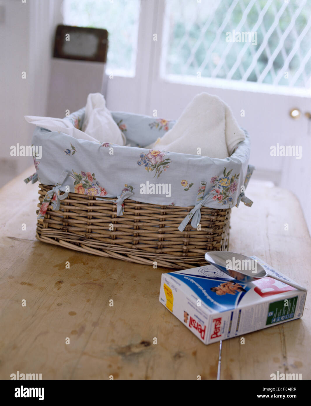 Nahaufnahme einer Waschmaschine Korb mit geblümten Stoffen auf Tisch, gesäumt mit einer Packung Waschpulver Stockfoto