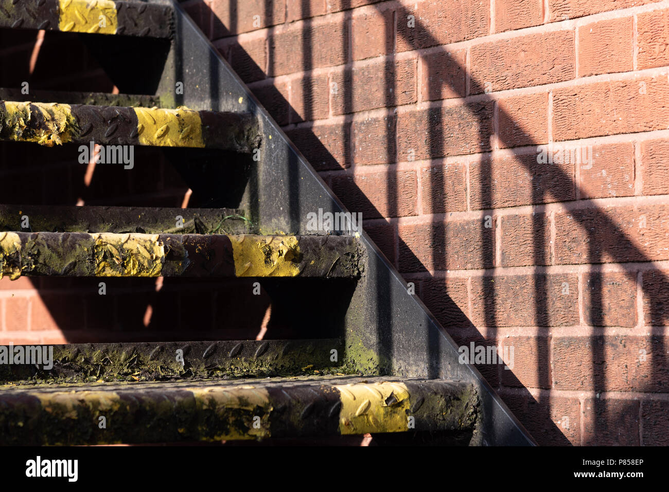 Nahaufnahme der Stufen mit schwarzen und gelben Warnstreifen. Verticalgestreifter Schatten, der durch Handlauf an die Wand geworfen wird Stockfoto
