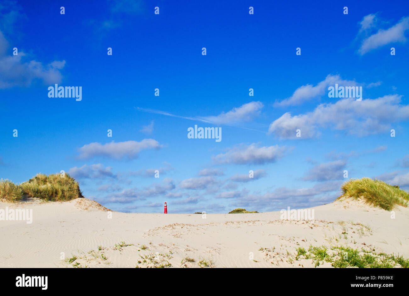 Dünen von der holländischen Insel Schiermonnikoog, in der Ferne die roten Leuchtturm, unter einem blauen Himmel mit einigen Wolken Stockfoto