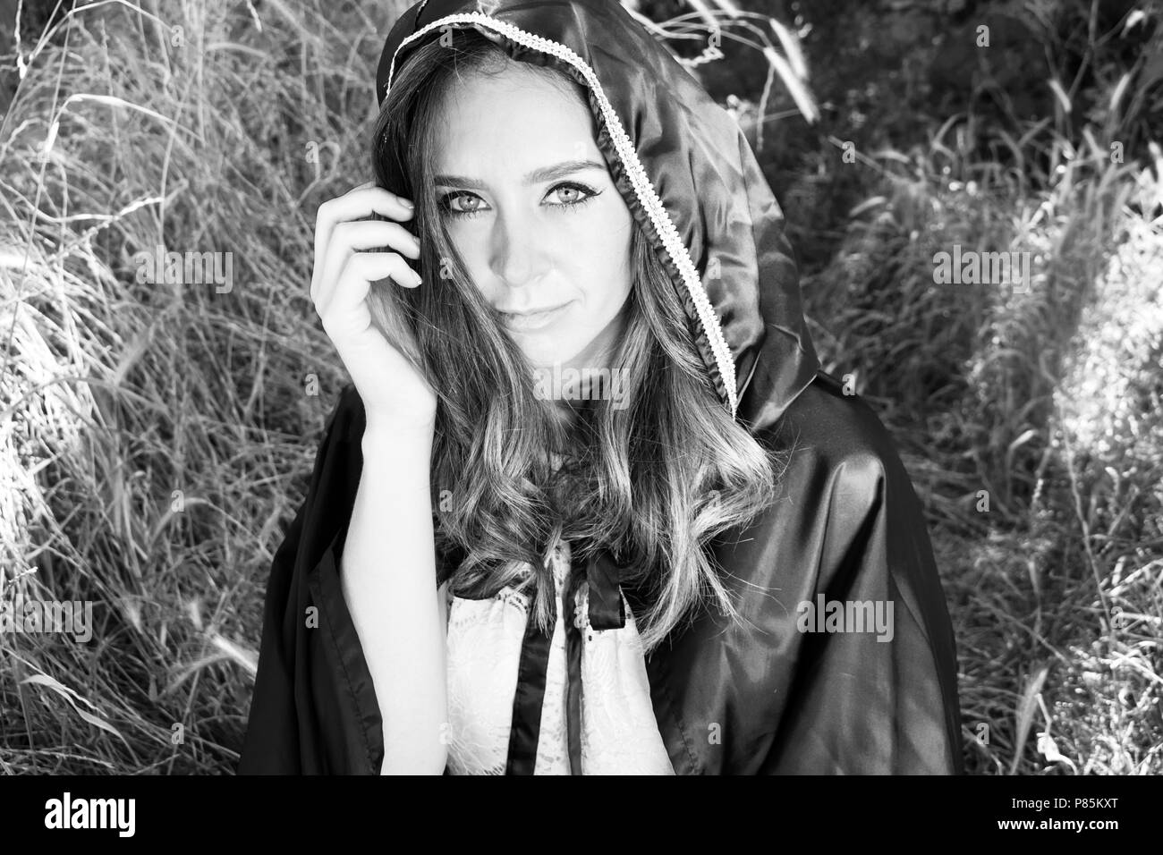 Schöne Frau hält Kapuze über Ihr braunes Haar wie Ihre blauen Augen in die Kamera schauen. Mit Wald und Bäume im Hintergrund. Stockfoto