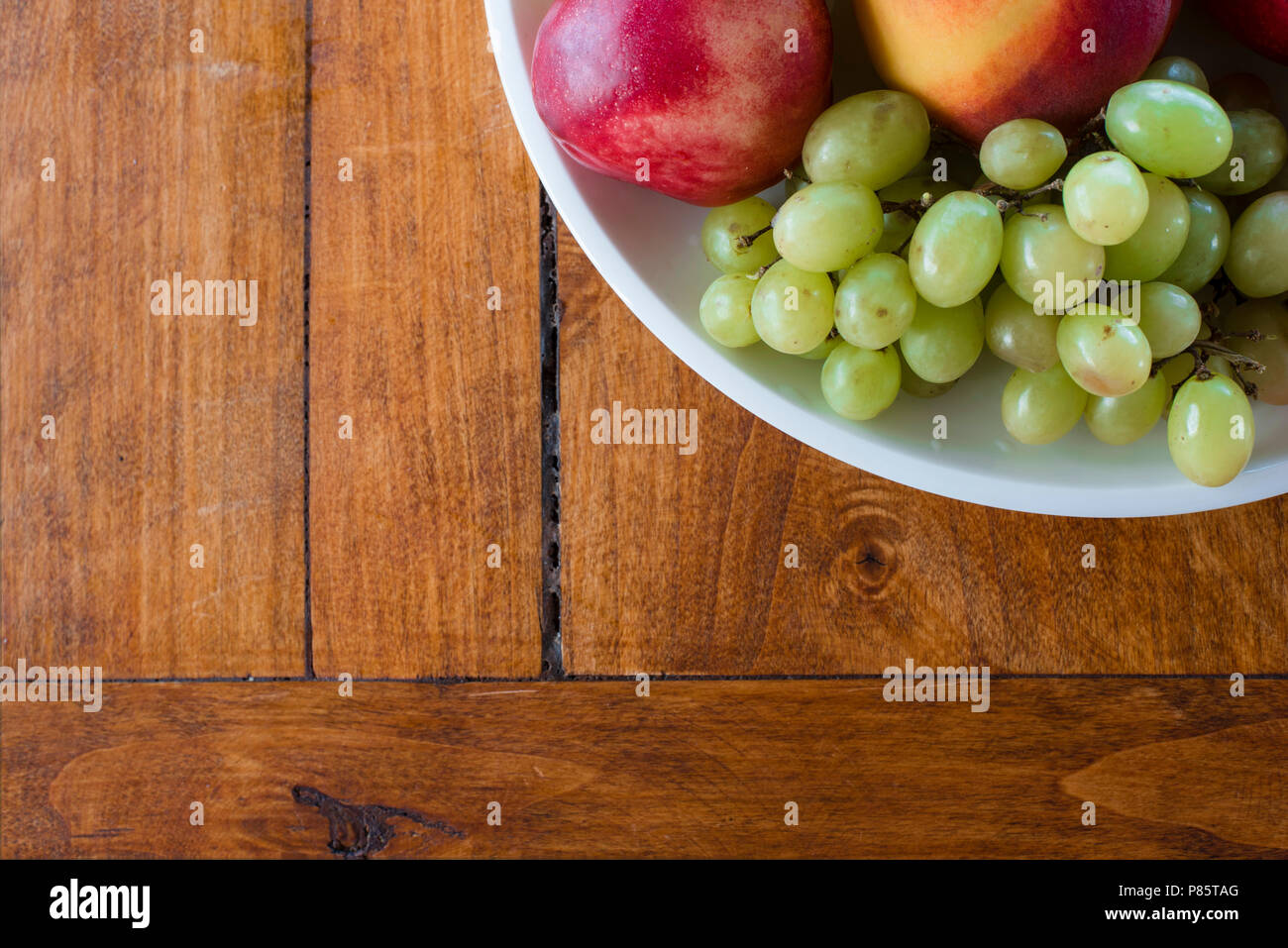 Schale mit Apfel-, Pfirsich- und Trauben von oben Blickwinkel auf Holz Textur Hintergrund gedreht. Gesunde Bio-Lebensmittel in hölzernen Tisch, mit Kopie Raum Stockfoto