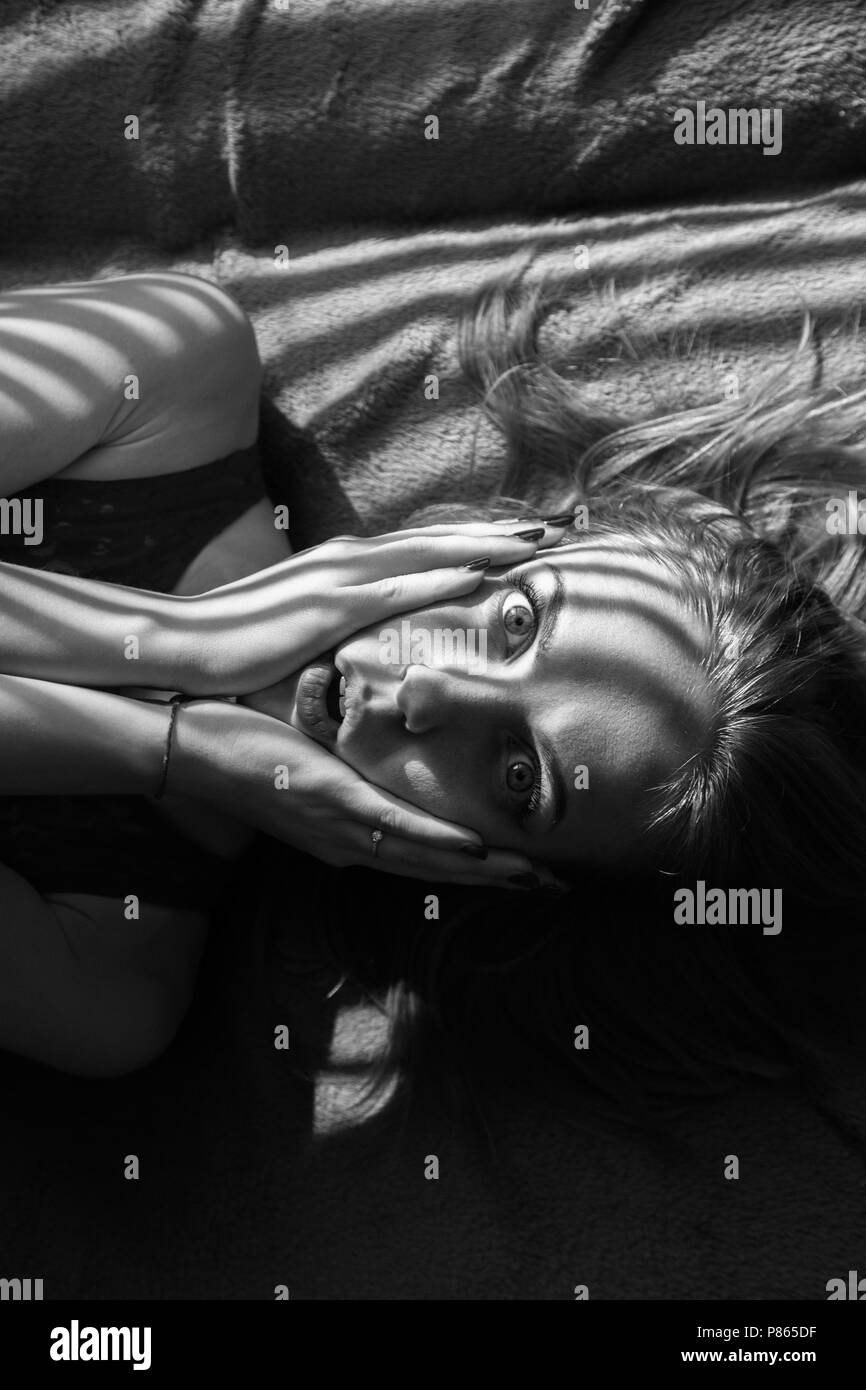 Angst Mädchen liegt auf dem Bett im Sonnenlicht mit Jalousien Schatten, Monochrom Stockfoto