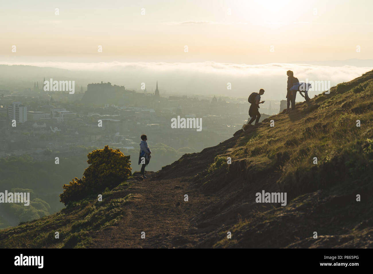 Touristen zu Fuß in der Nähe von Salisbury Craigs in Edinburgh, Schottland, mit Meer Nebel (5,2Km) im Hintergrund, kurz vor Sonnenuntergang. Stockfoto