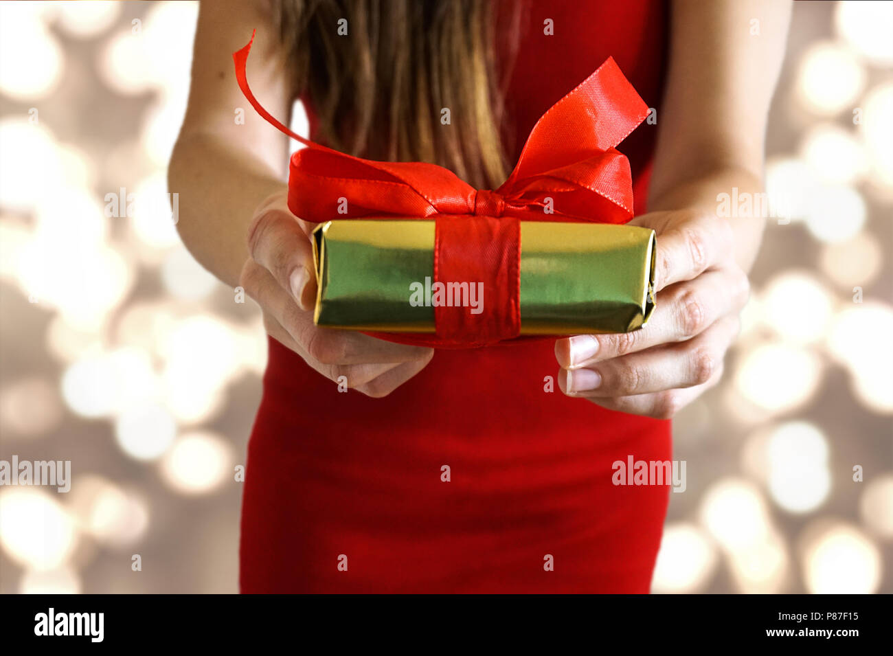 Weibliche Hände geben ein Geschenk mit roter Schleife für Valentines Tag/Geburtstag/Weihnachten mit Golden Lights Hintergrund Stockfoto