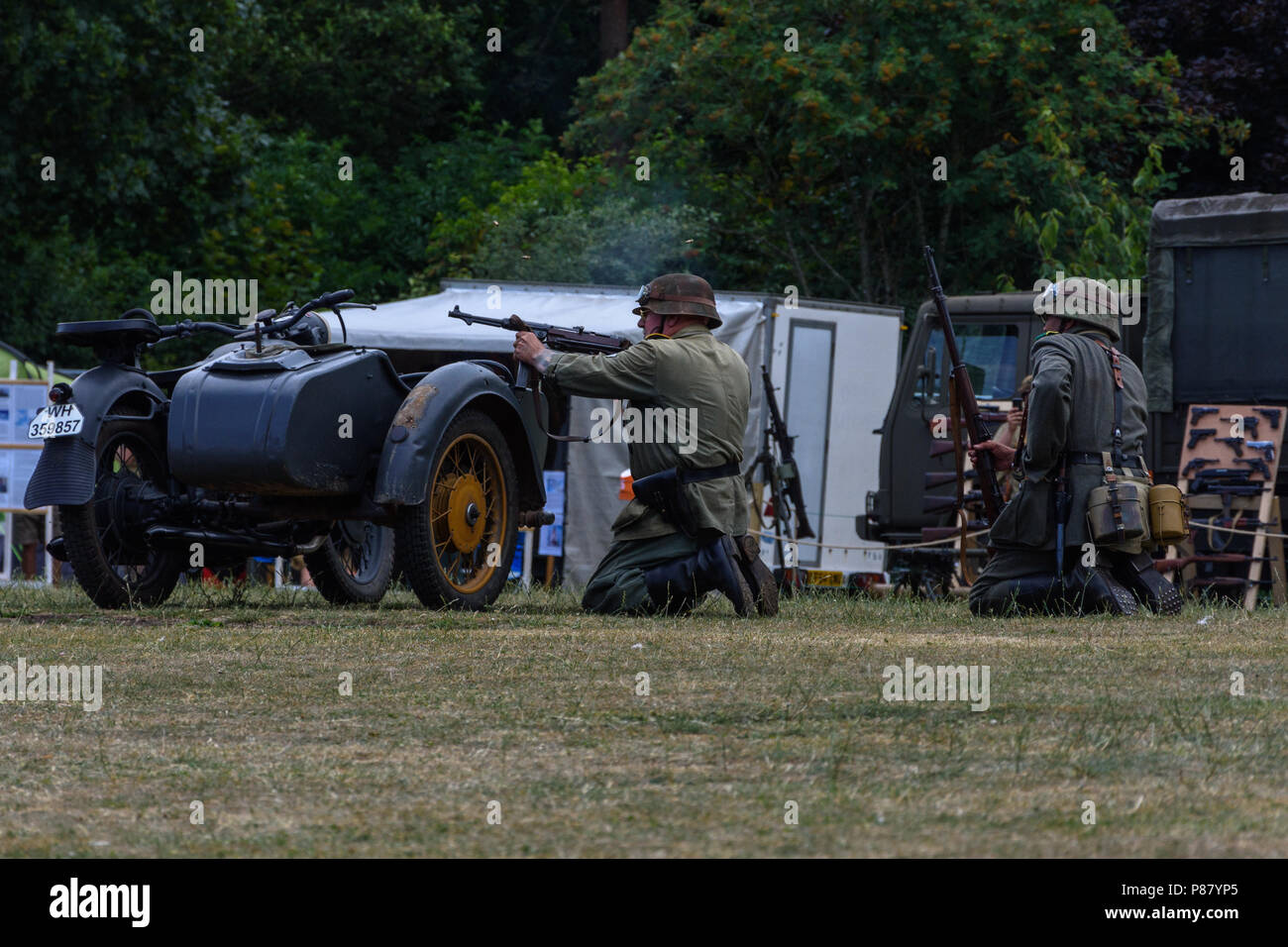 2 Schauspieler NS-Soldaten schießen über ein Motorrad und seitenwagen als Deckung während einer zweiten Weltkrieg skirmish Re-enactment für Streitkräfte Tag Stockfoto