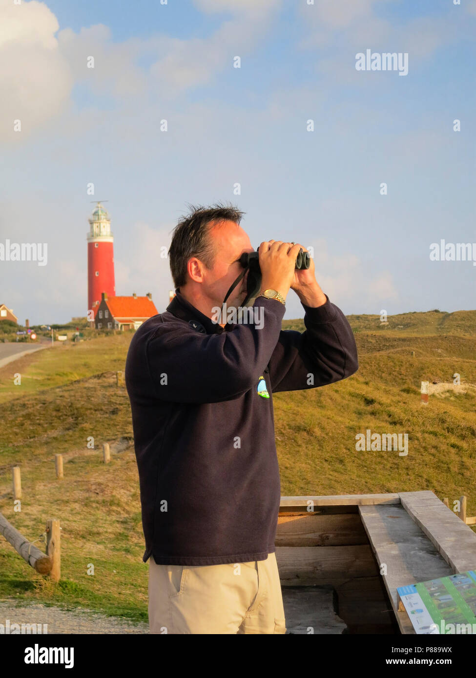 Man met Verrekijker op uitkijkpunt met vuurtoren in Achtergrond; Mann mit Fernglas an View Point mit Leuchtturm im Hintergrund Stockfoto