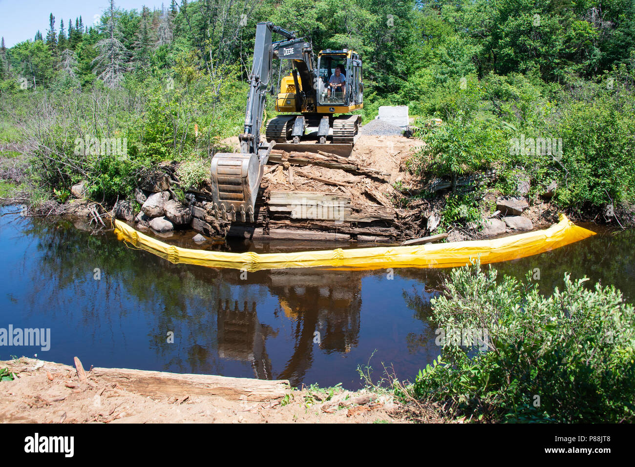 Eine Spur hoe Maschine mit einem Operator eine neue Brücke über den Fluss Kunjamuk in den Adirondack Mountains, NY, USA Stockfoto