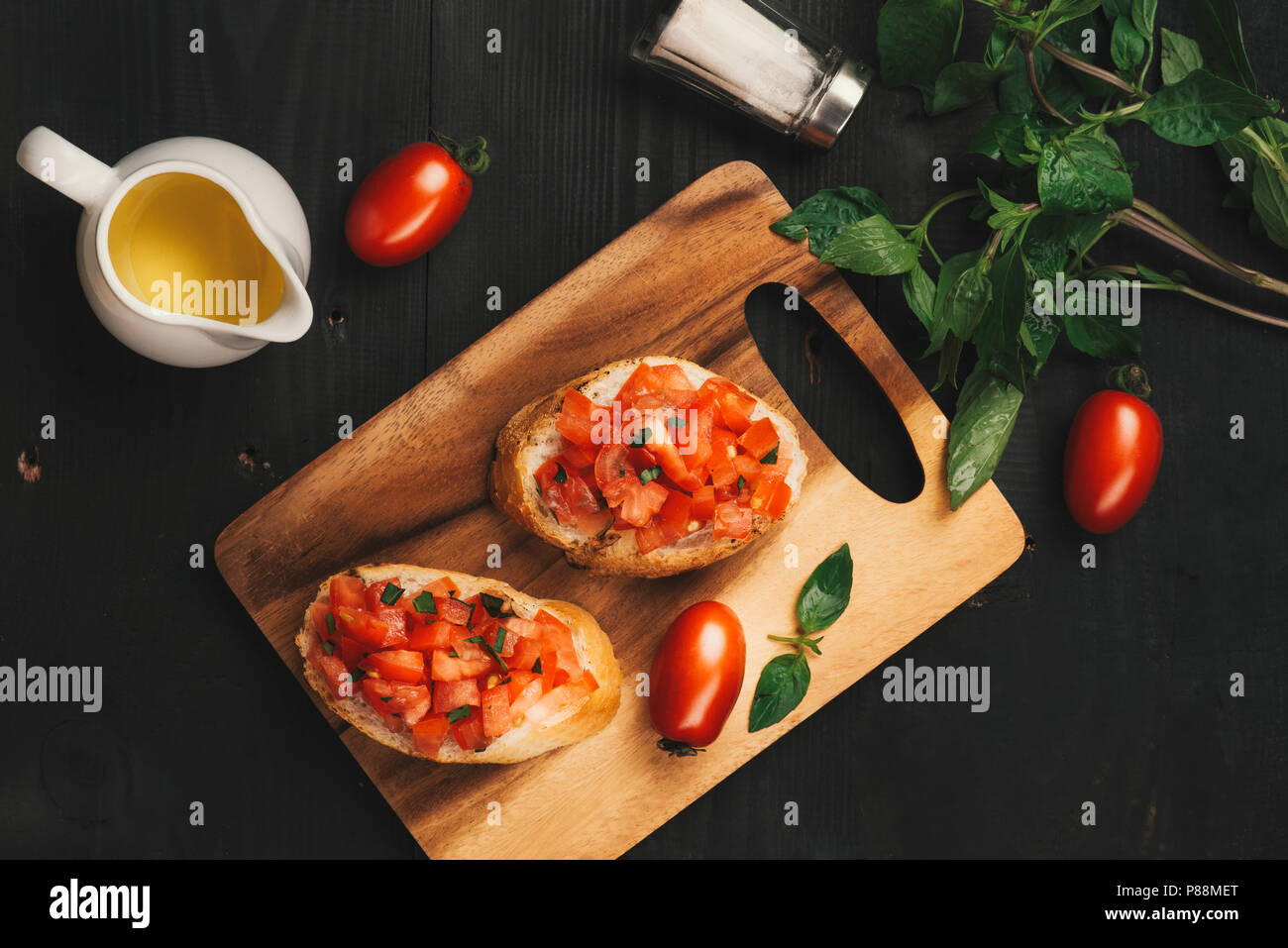 Leckere italienische Bruschetta mit Brot garniert mit Tomaten und Kräutern auf Holzbrett Stockfoto