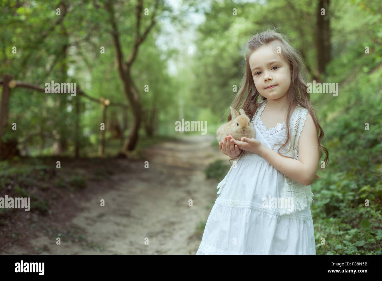 Kleine Mädchen in den Märchenwald. Sie hält ein kleines Kaninchen in ihren Händen. Stockfoto