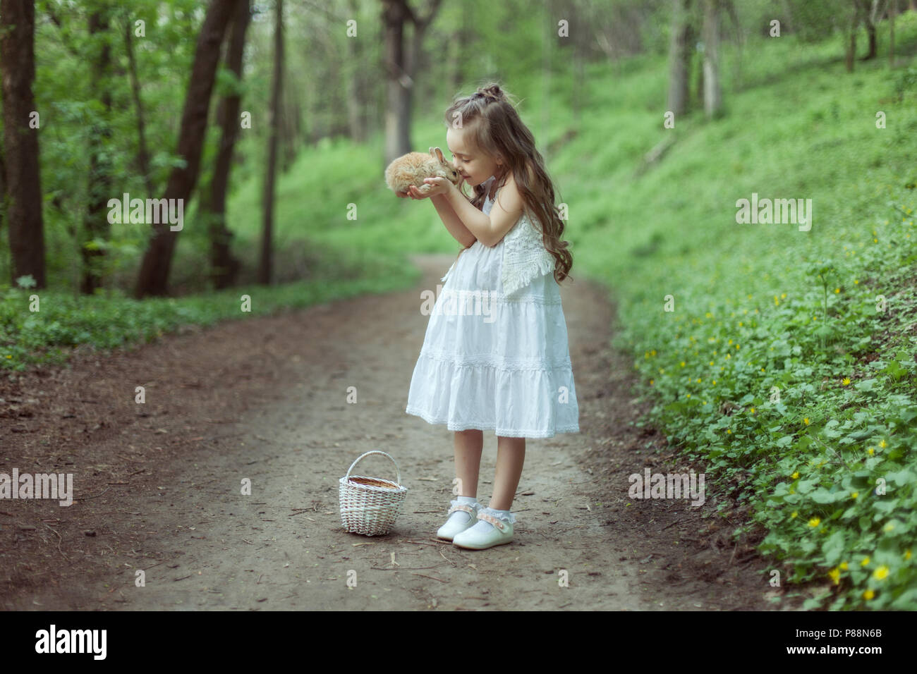 Porträt eines kleinen Mädchens im Wald. Sie hält ein kleines Kaninchen in ihren Händen. Stockfoto