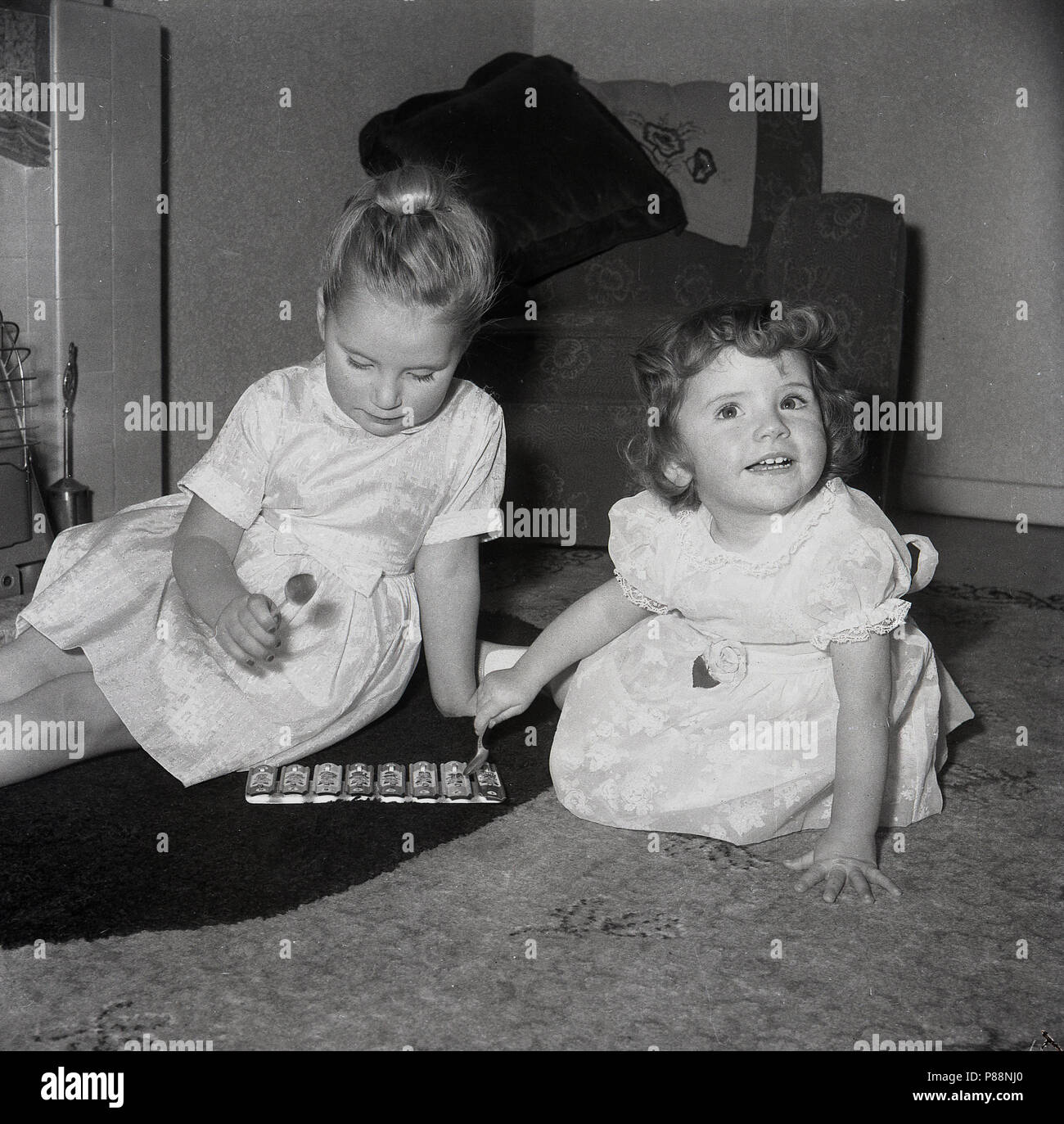 1950, historische, zwei junge Mädchen zusammen sitzen auf dem Boden eines Wohnzimmer spielen mit einem kleinen musikalischen Spielzeug, ein Metall, Xylophon, Stockfoto