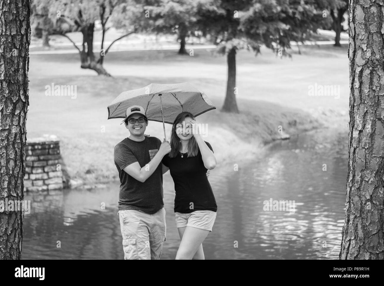 Junge Glücklich attraktives Paar draußen im Park mit Regenschirm und Bäume im Hintergrund Stockfoto