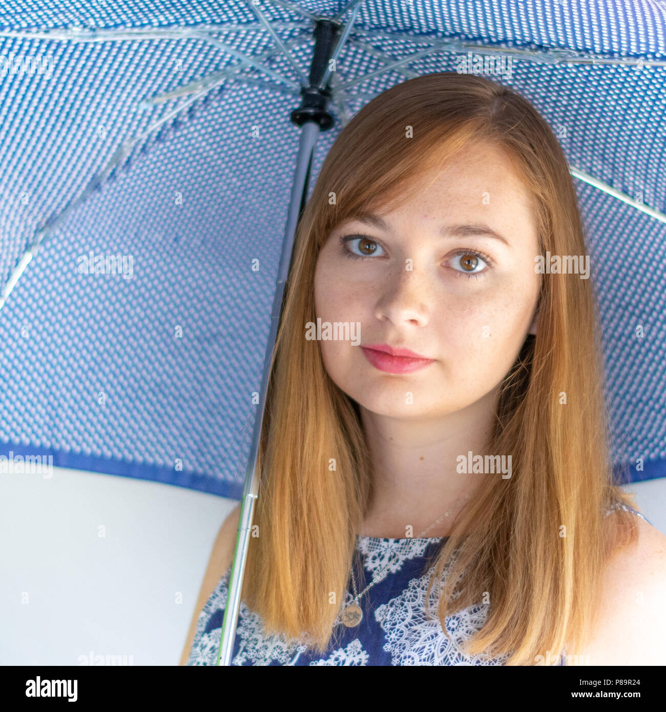 Hübsche rothaarige Frau mit blauen Kleid und Holding blau Regenschirm Stockfoto