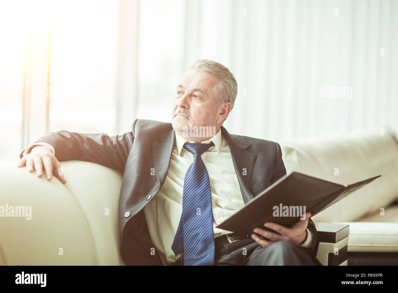 Erfolgreicher Geschäftsmann erwägt, einen neuen Vertrag auf dem Sofa sitzen im eigenen Büro Stockfoto
