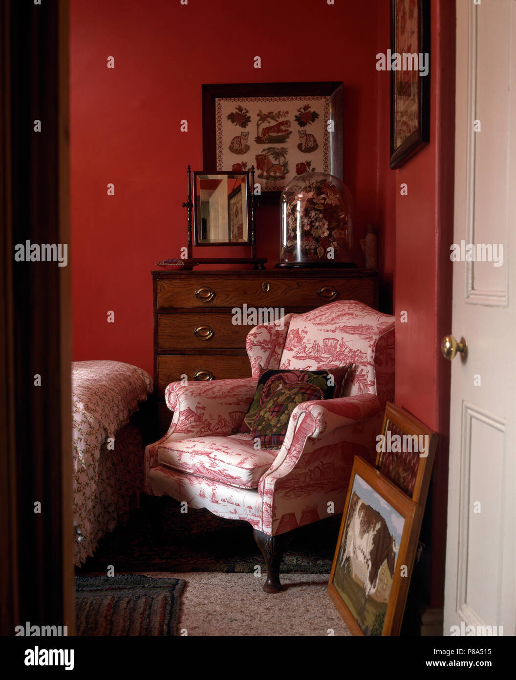 Rosa Toile-de-Jouy Sessel gegen die Brust-of-Schubladen mit einer viktorianischen Glaskuppel in einem kleinen Tief rosa Schlafzimmer Stockfoto