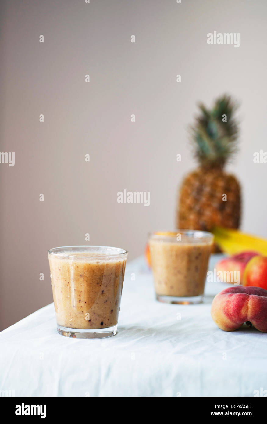 Gesunde Rohstoffe veganes Essen kochen Hintergrund. Frische Früchte und Smoothies am Tisch über weiße Tischtuch. Sauber Essen, basische Ernährung Konzept Stockfoto