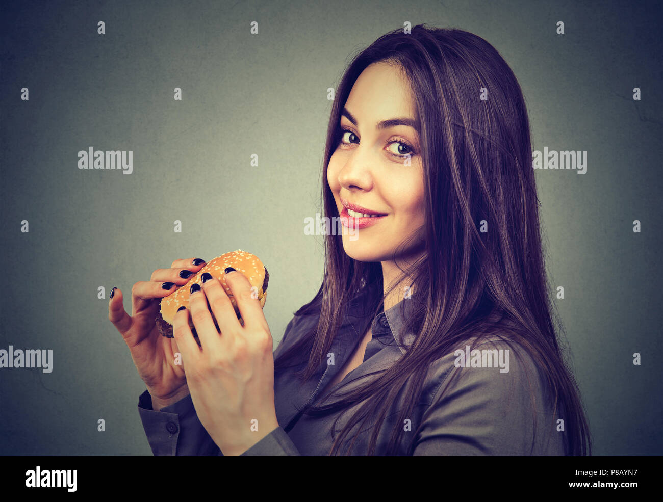 Schöne Frau mit einem Cheeseburger bei Kamera schaut Süß Stockfoto