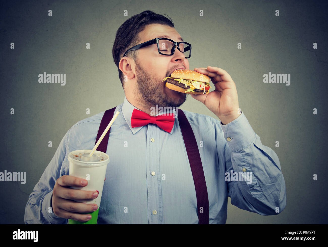 Übergewicht business Mann essen mit Appetit ein Burger Holding eine große Dose Soda drink Stockfoto