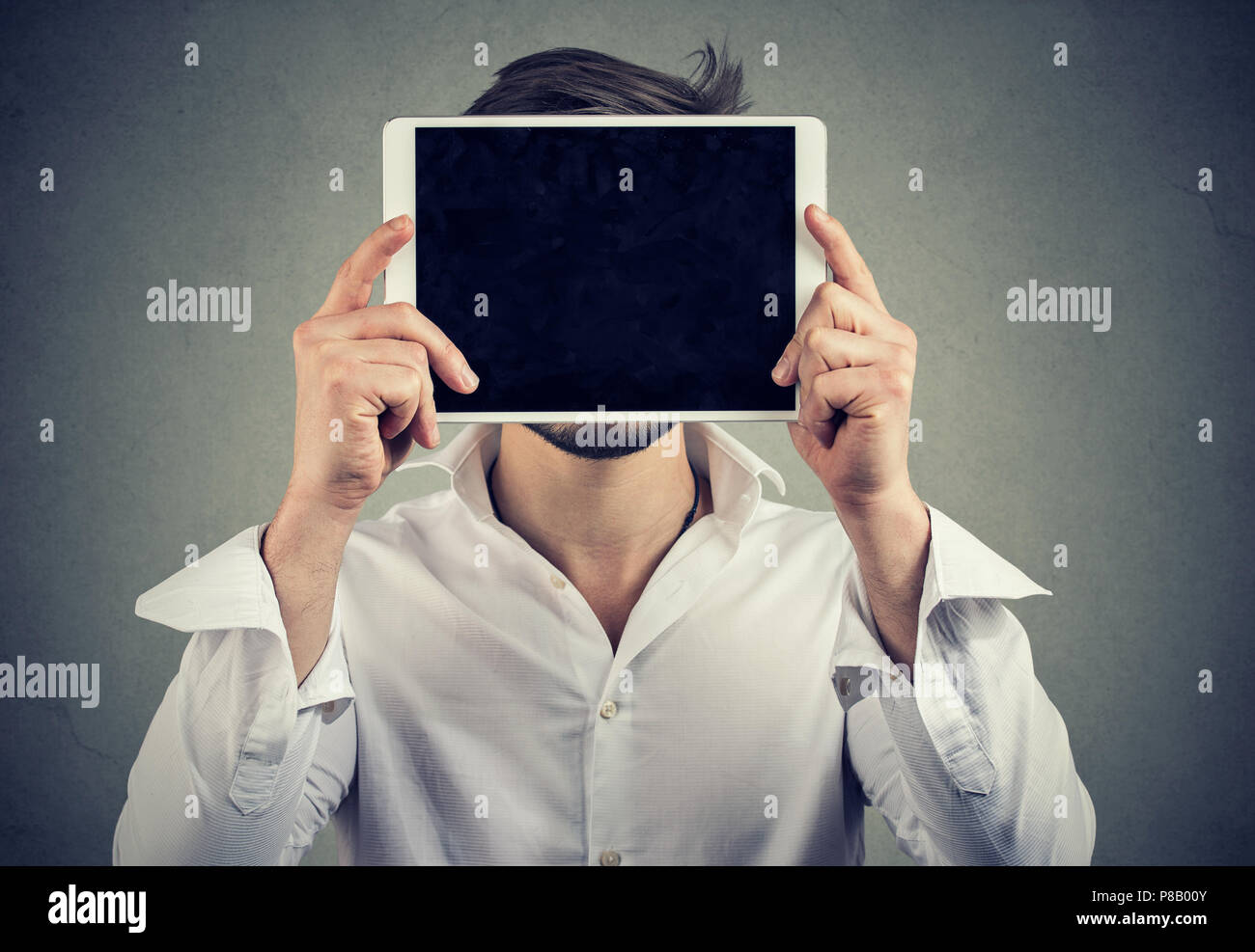 Anonyme Mann im weißen Hemd holding Tablet vor Gesicht inkognito in sozialen Medien auf grauem Hintergrund Stockfoto
