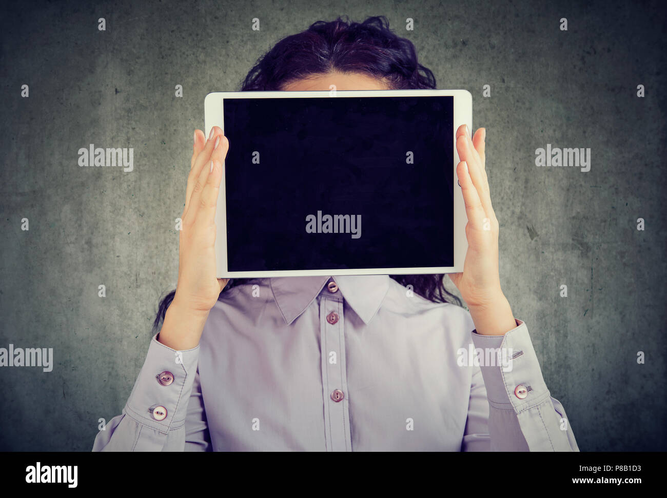 Anonymer brunette Frau in Shirt holding Tablet vor ihrem Gesicht, inkognito in sozialen Medien auf grauem Hintergrund Stockfoto