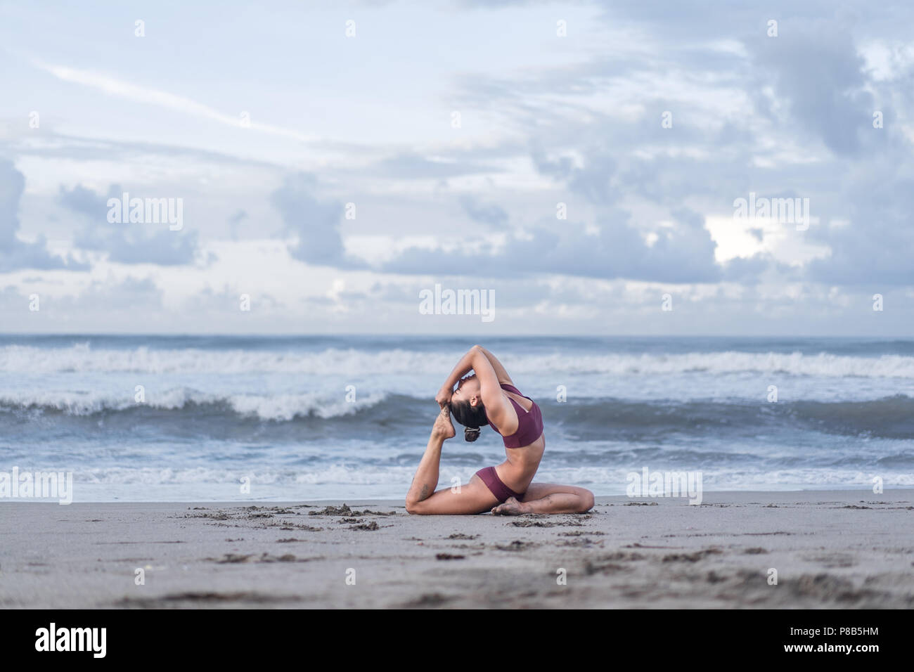 Seitenansicht der jungen Frau Yoga in einem vierbeinigen König Taube darstellen (Eka Pada Rajakapotasana) an der Küste Stockfoto