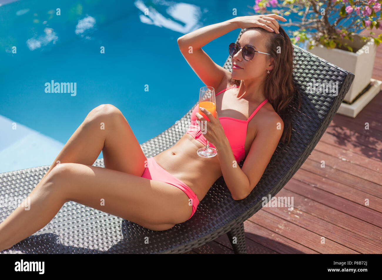 Junge Frau im Bikini in der Sonne liegend Lounge mit Cocktail am Pool  Stockfotografie - Alamy