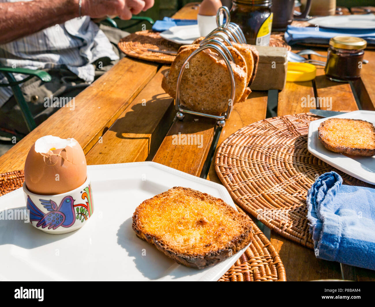 Mann essen Frühstück im Freien während der Sommerhitze, mit gekochtem Ei und Toast im Rack auf hölzernen London Garten Tisch Stockfoto