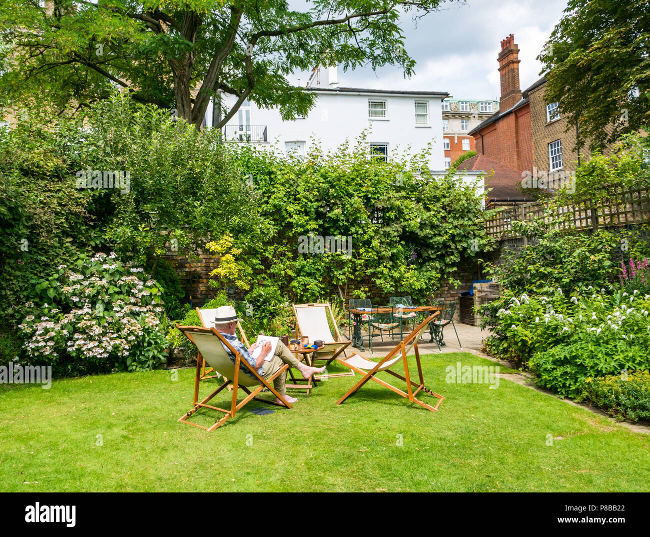 Ältere Mann, der Panama Hut Lösung Kreuzworträtsel im Liegestuhl sitzen im großen Garten in Sommerhitze, London, England, Großbritannien Stockfoto