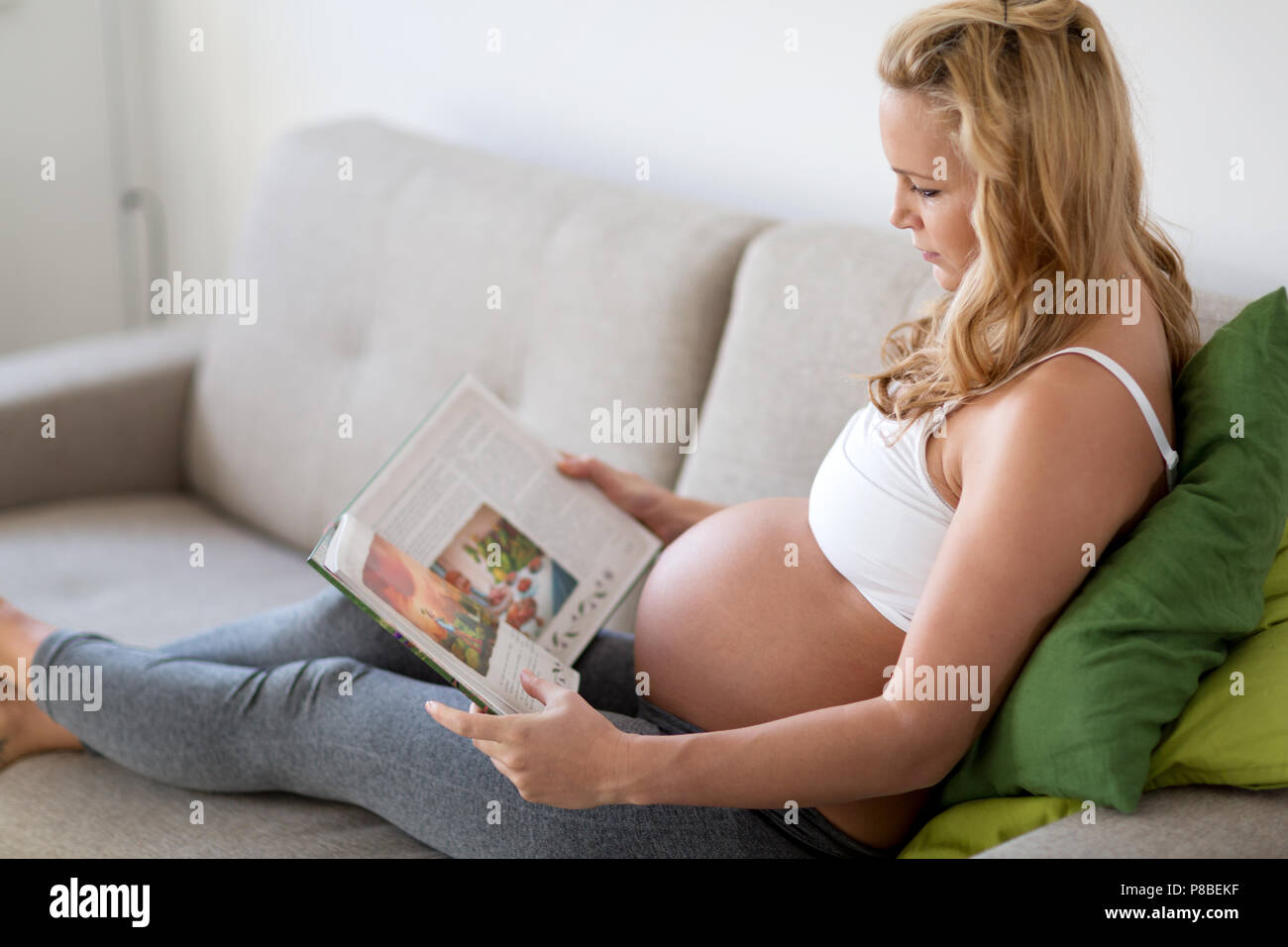 Schwangere Frau ausruhen und lesen Buch auf dem Sofa Stockfoto