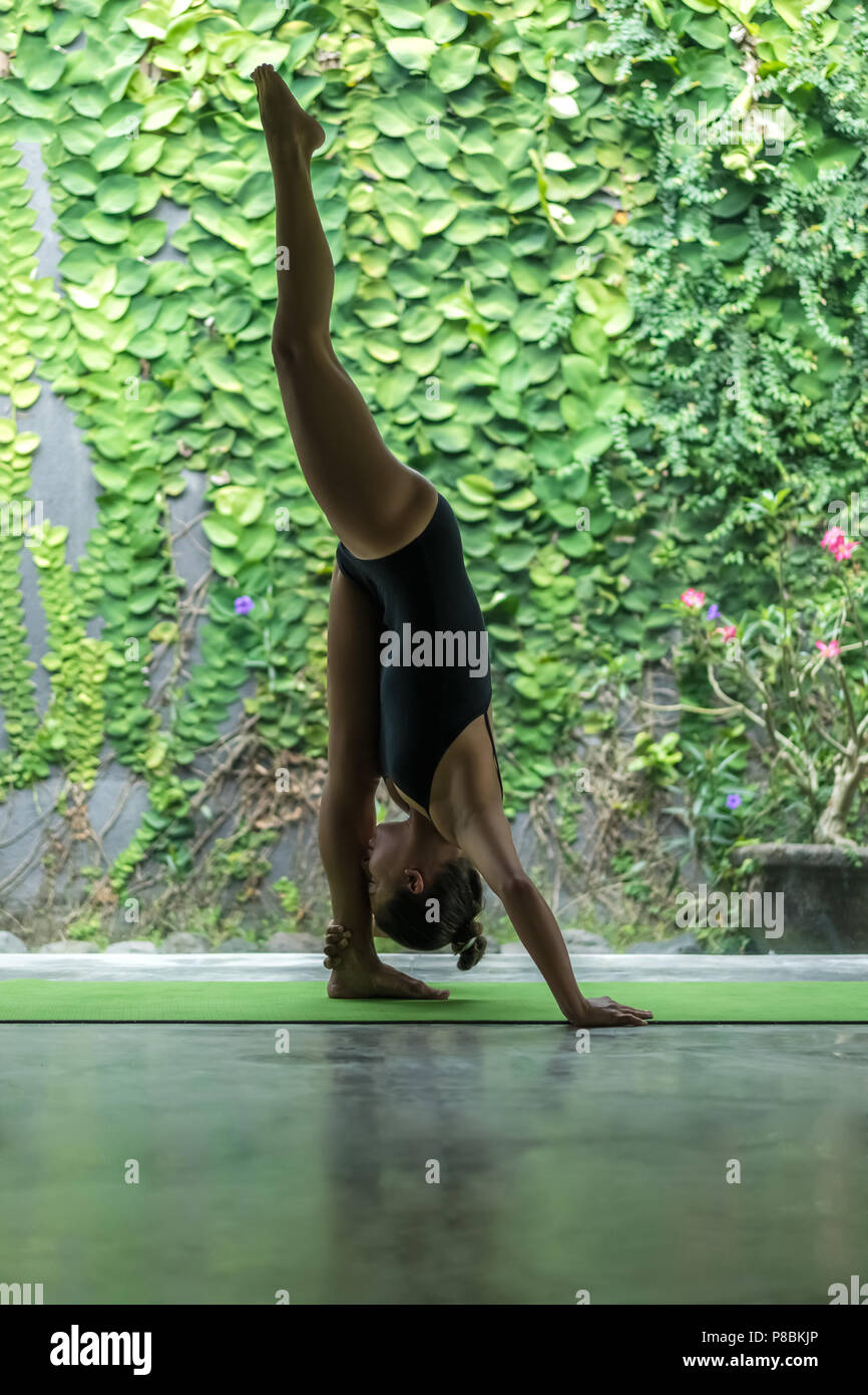 Seitenansicht der sportliche junge Frau Yoga in ständigen Splits darstellen (Urdhva Prasarita Eka Padasana) vor der Wand mit grünen Blättern bedeckt Stockfoto