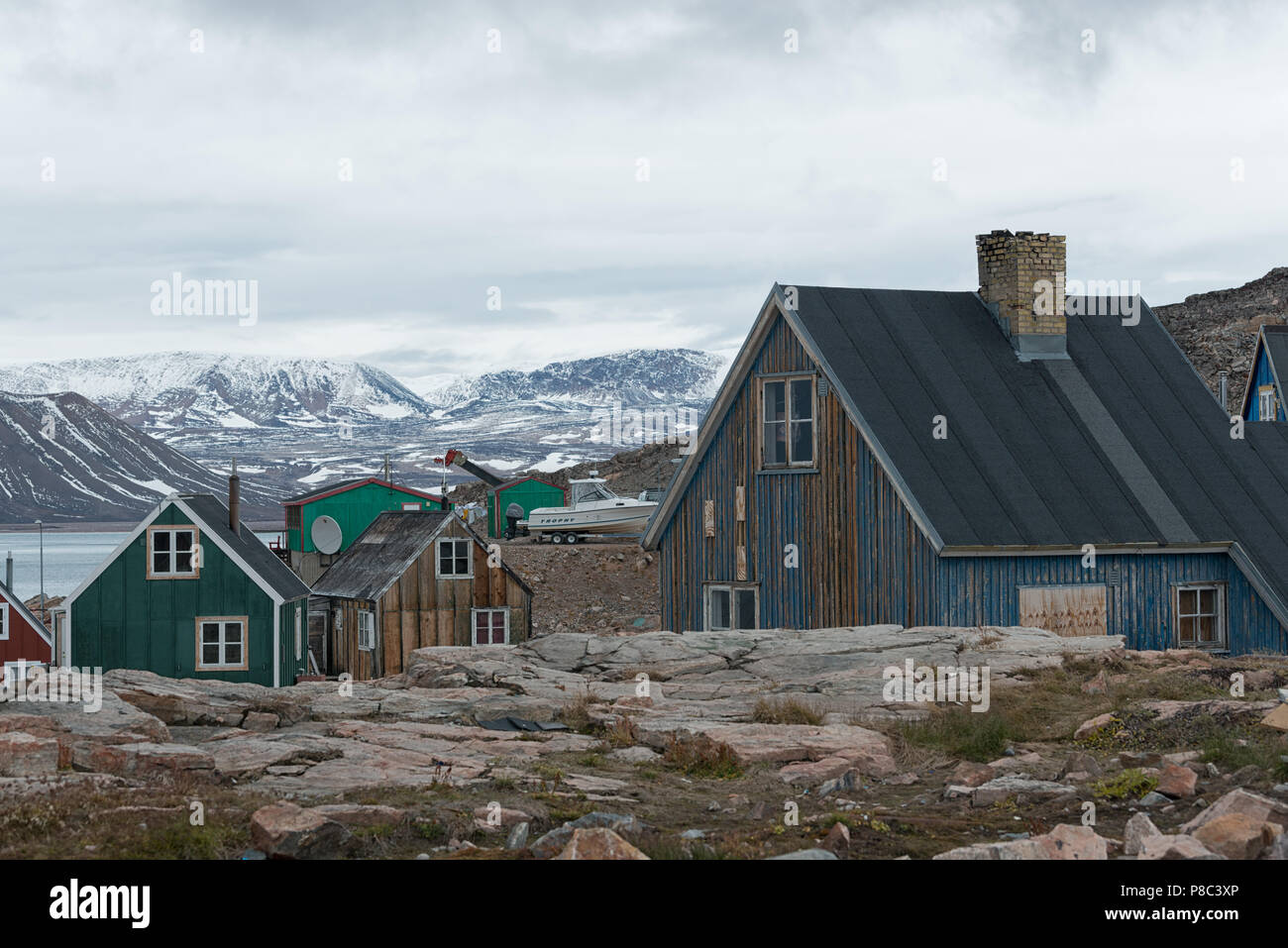 Bunte Holzhäuser mit schneebedeckten Bergen dahinter im Herbst, Ittoqqortoormiit, Liverpool Land, Ostgrönland, Königreich Dänemark Stockfoto