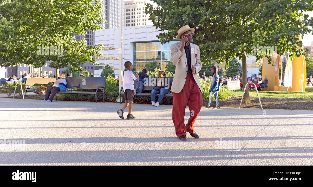 Ein älterer Rapper spricht Black man per Handy an, während er durch das Einkaufszentrum im Freien in der Innenstadt von Cleveland, Ohio, USA läuft. Stockfoto