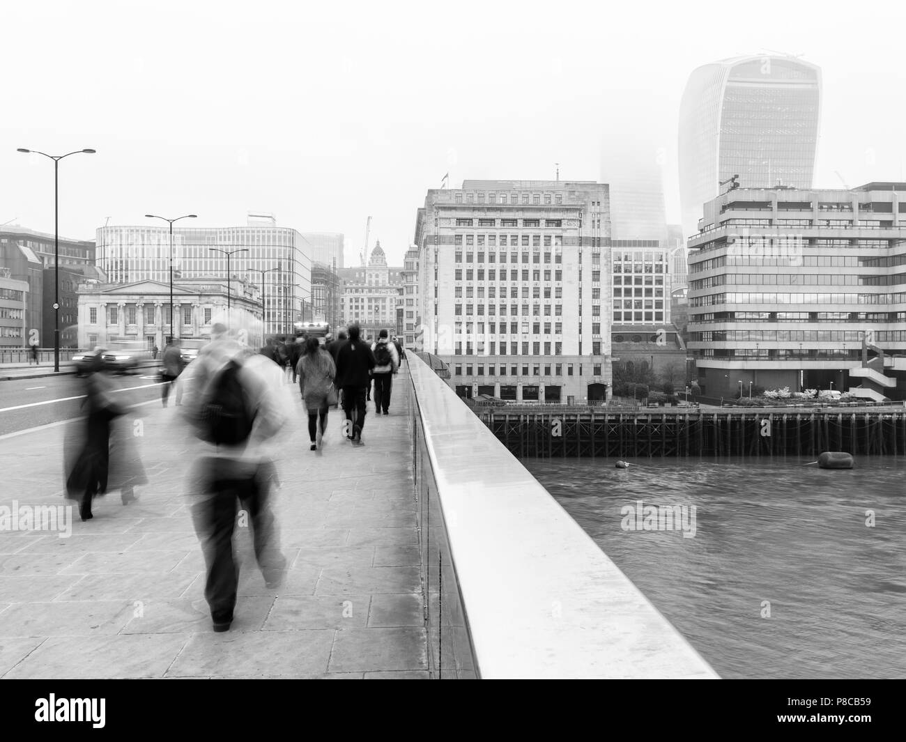 Montag morgen Pendler gehen auf die London Bridge über der Themse und gegenüber der City und Walkie Talkie Gebäude auf einem nebligen Tag arbeiten. Stockfoto