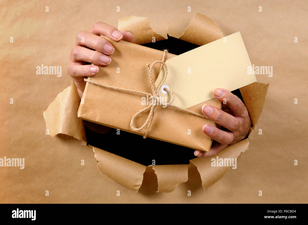 Man Hände liefern oder das Paket durch zerrissene braunes Papier Hintergrund Stockfoto