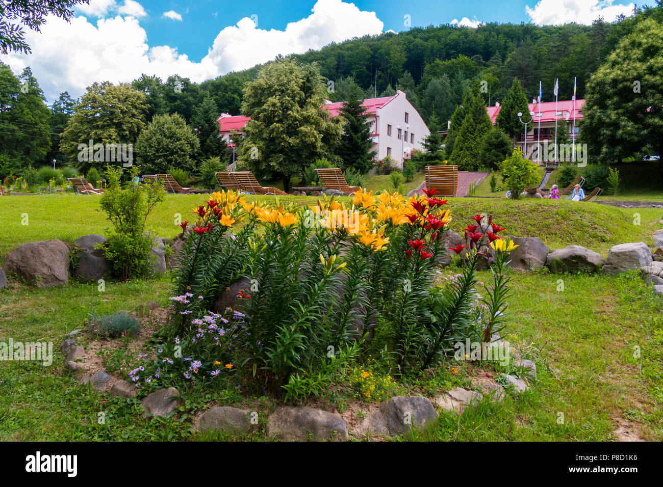 Blumenbeet mit rot und orange Lilien auf einem hohen grünen Bein vor dem Hintergrund der Gebäude der Hotel Komplex. Für ihr Design Stockfoto