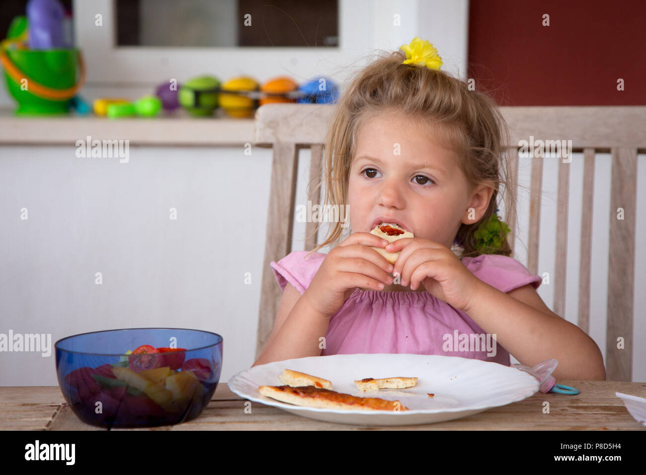 Mädchen von 2 und eine Hälfte isst ein Stück Pizza im Freien zu Hause Stockfoto