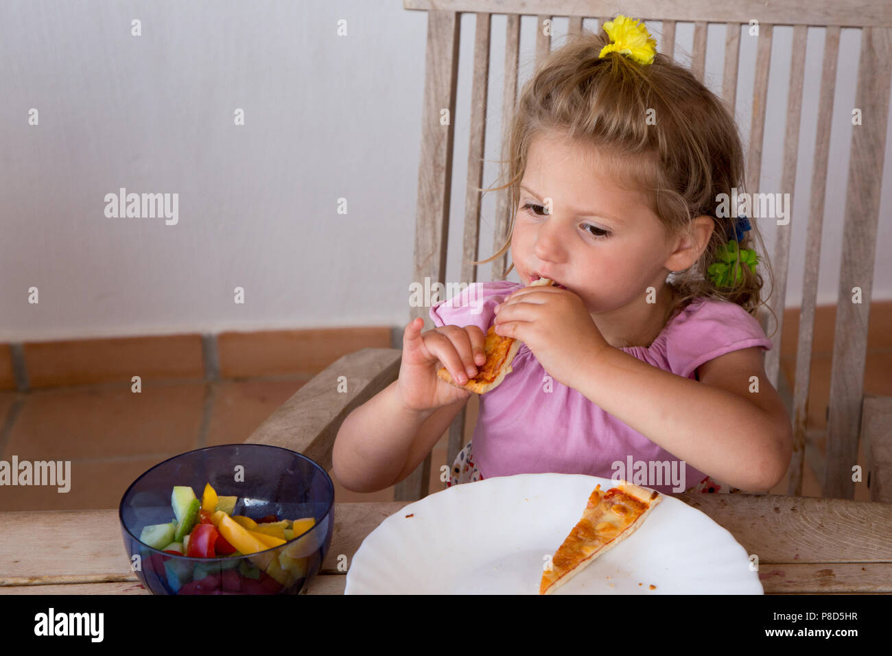 Mädchen von 2 und eine Hälfte isst ein Stück Pizza im Freien zu Hause Stockfoto